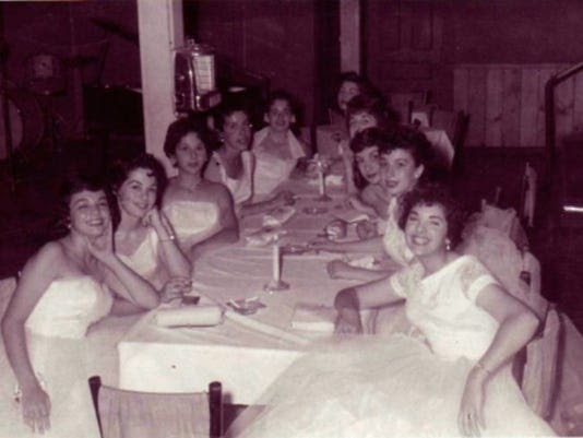 A group of young women in white dresses sit at a long banquet table.